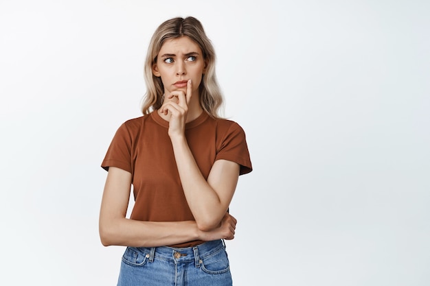 Portrait of concerned woman looking hesitant aside, thinking of something, standing on white