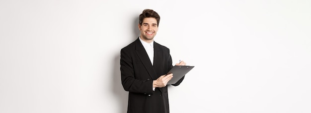 Free photo portrait of confident businessman in black suit signing documents and smiling standing happy against