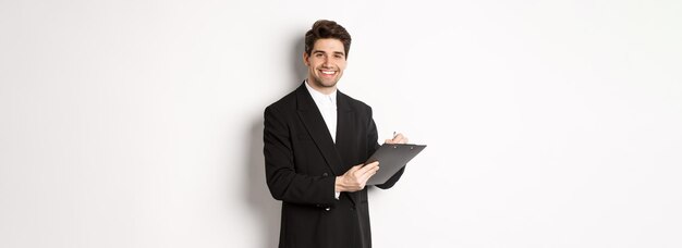 Free photo portrait of confident businessman in black suit signing documents and smiling standing happy against