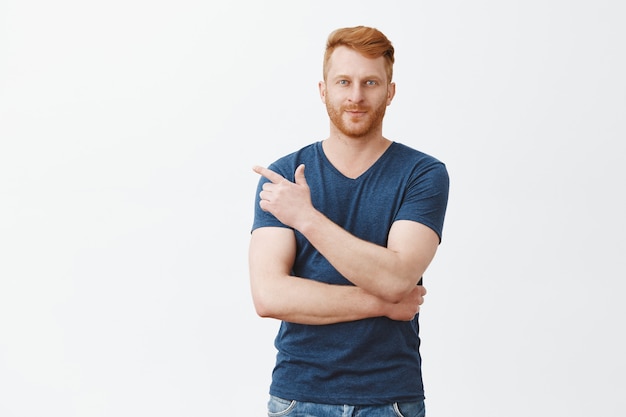 Portrait of confident charming redhead caucasian guy with bristle in casual outfit, pointing at upper left corner