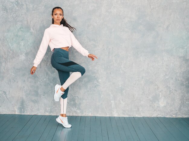 Portrait of confident fitness woman in sports clothing looking confident.Female jumping in studio near gray wall