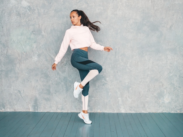 자신감을 찾고 스포츠 의류에 자신감이 피트 니스 여자의 초상화 회색 벽 근처 스튜디오에서 점프 여성