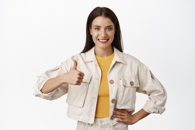 Portrait of confident girl show thumb up and nod in approval, say yes, praise and agree, recommend excellent brand product, compliment great choice, white background