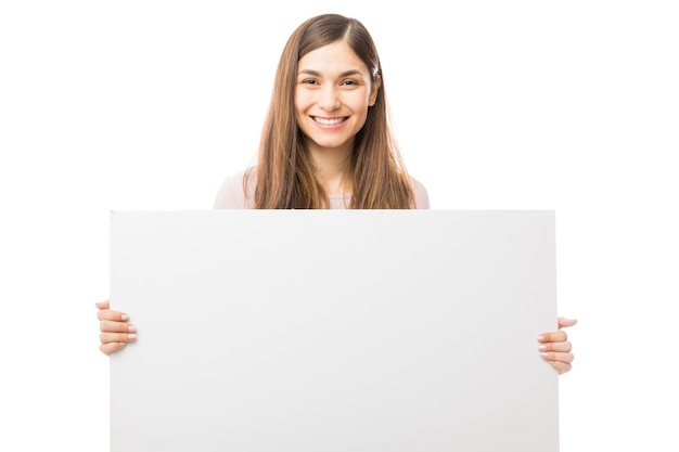 Портрет уверенной в себе счастливой женщины, держащей пустой рекламный щит на белом фоне