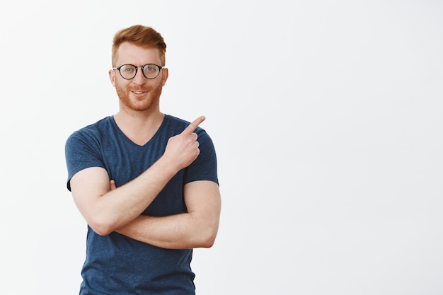 Portrait of confident masculine and smart redhead male with bristle in glasses, pointing at upper right corner