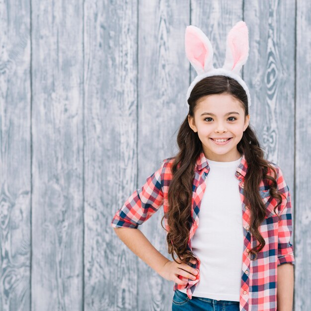 Портрет уверенно улыбается девушка с ухом кролика на голове на деревянном фоне