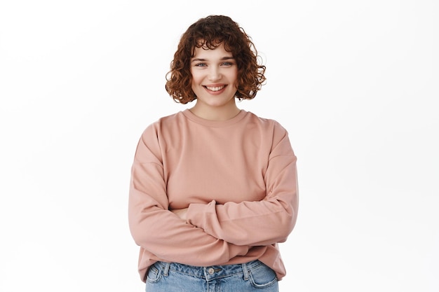 Free photo portrait of confident smiling young woman, cross arms on chest, smiles and looks with determines and self-assured expression, standing over white background.