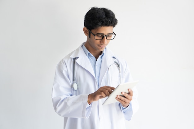 Free photo portrait of confident young doctor in glasses using pc tablet.