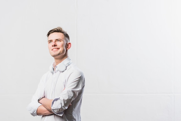 Portrait of confident young man with headphone around his neck standing with his arms crossed against white wall