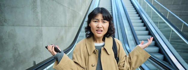 Портрет растерянной азиатской девушки, которая не знает, где она потерялась в незнакомом городе, спускается по эскалатору