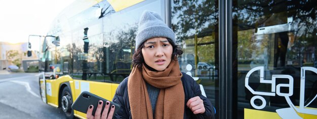 ショックを受け動揺しているように見える携帯電話を持ってバス停に立っている混乱したアジアの女の子の肖像画