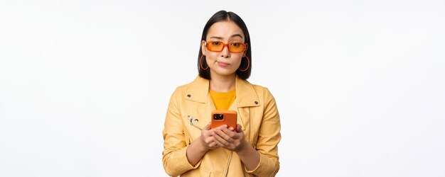 휴대폰을 사용하여 스마트폰을 들고 퍼즐을 찾고 있는 선글라스를 끼고 혼란스러워하는 아시아 소녀의 초상화