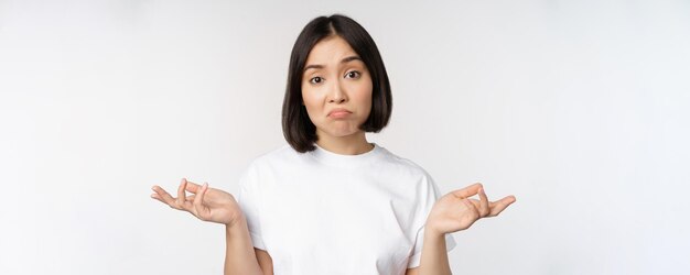 Portrait of confused asian woman shrugging shoulders looking clueless puzzled to say standing over white background