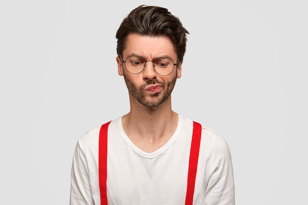 Free photo portrait of confused bearded man frowns face, looks with puzzled expression, concentrated down