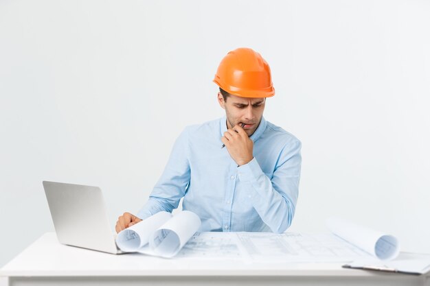 Portrait of confused male designer or architect, feels stressed, being nervous, keeps hand on head, stares in blueprint. Exhausted man creates construction project alone, has some troubles.