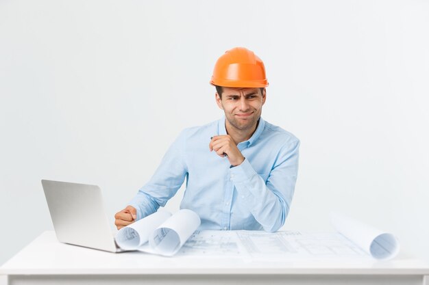 Portrait of confused male designer or architect, feels stressed, being nervous, keeps hand on head, stares in blueprint. Exhausted man creates construction project alone, has some troubles