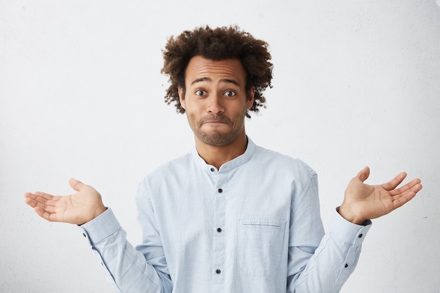 Free photo portrait of confused male standing against white studio wall shrugging his shoulders