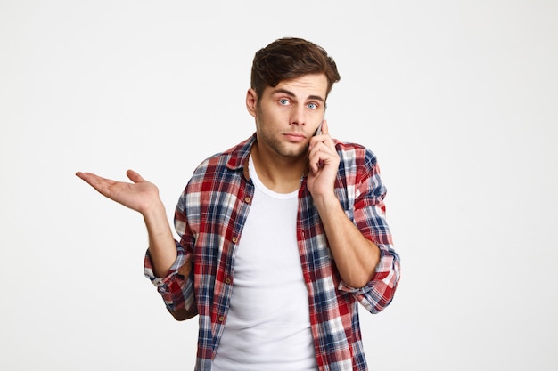 Portrait of a confused puzzled man talking on mobile phone