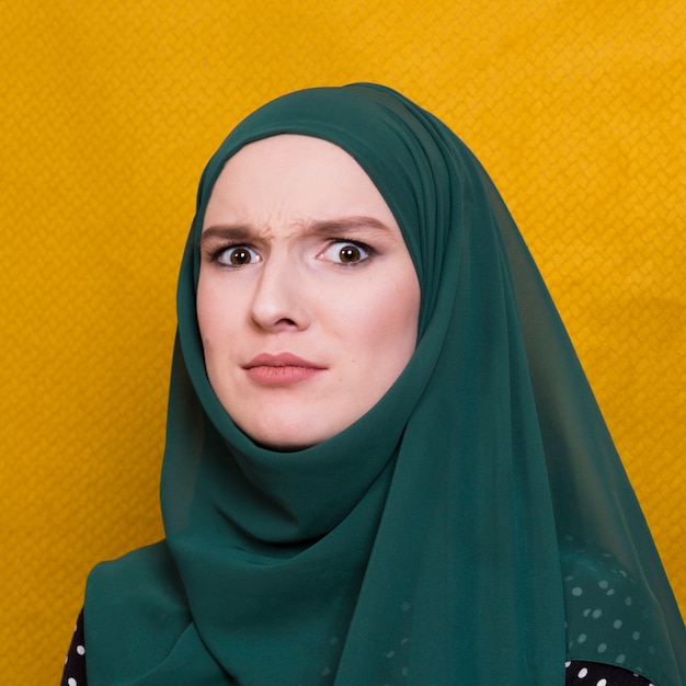 Portrait of confused woman looking at camera against yellow backdrop