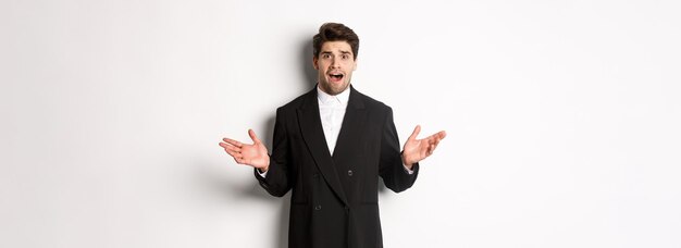 Portrait of confused and worried handsome man in suit looking at something strange spread hands side