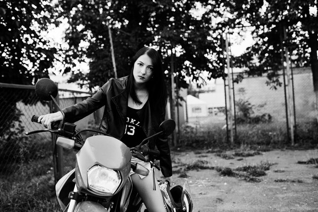 Portrait of a cool and awesome woman in dress and black leather jacket sitting on a cool red motorbike Black and white photo