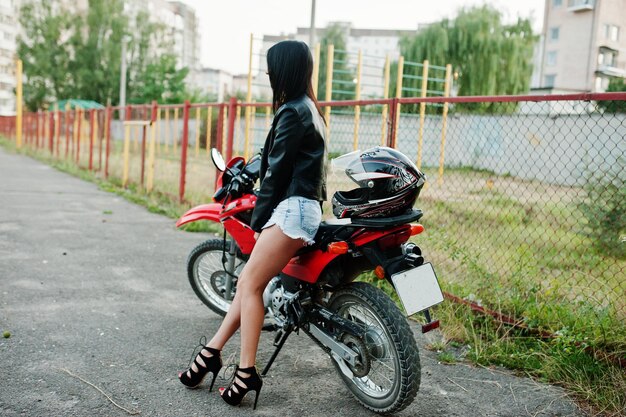 멋진 빨간 오토바이에 앉아 있는 드레스와 검은 가죽 재킷을 입은 멋지고 멋진 여성의 초상화