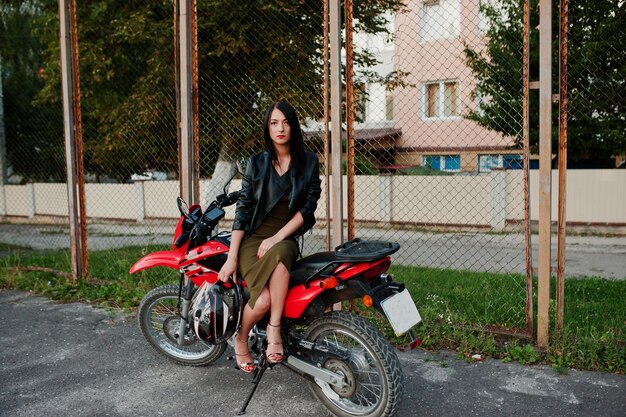멋진 빨간 오토바이에 앉아 있는 드레스와 검은 가죽 재킷을 입은 멋지고 멋진 여성의 초상화