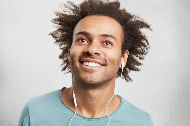 Portrait of cool young black man with curly hair, has cheerful expression