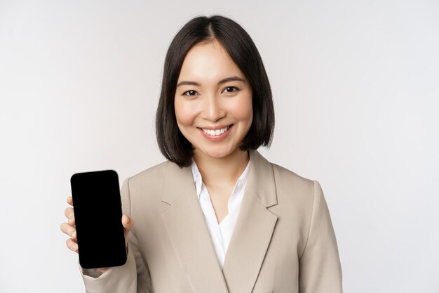 白い背景の上に立っているスマートフォンアプリインターフェイス携帯電話の画面を示す企業のアジアの女性の肖像画
