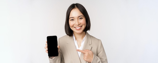 흰색 배경 위에 서 있는 스마트폰 앱 인터페이스 휴대폰 화면을 보여주는 기업 아시아 여성의 초상화