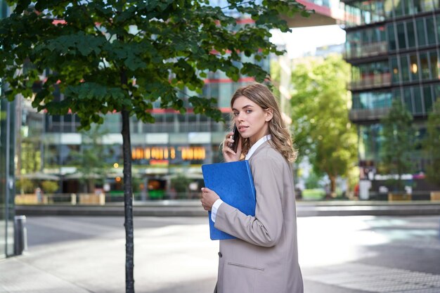 Portrait of corporate woman answers phone call while walking to the office building businesswoman ca