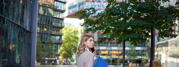 Free photo portrait of corporate woman answers phone call while walking to the office building businesswoman