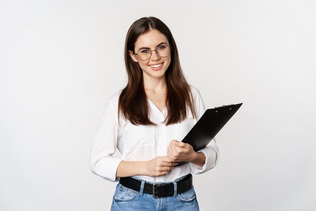 Portrait of corporate woman holding clipboard at work standing in formal outfit over white background