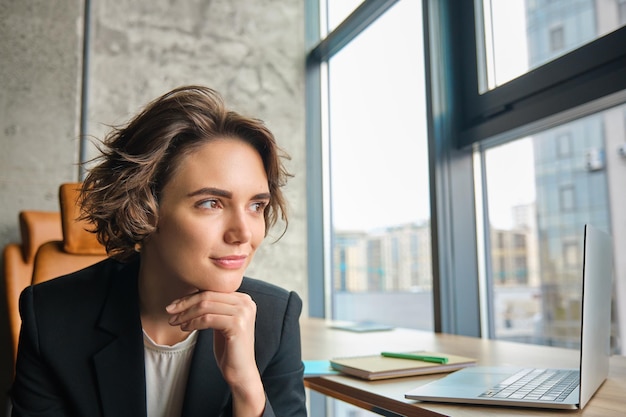 Free photo portrait of corporate woman looking outside window in her office smiling with confidence