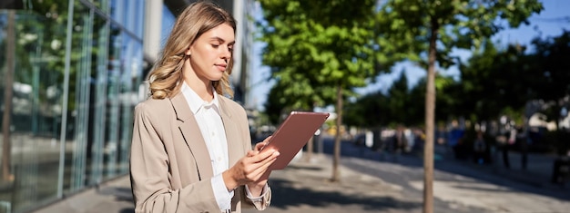 Free photo portrait of corporate woman reads news works on her digital tablet while on her way to office stansd