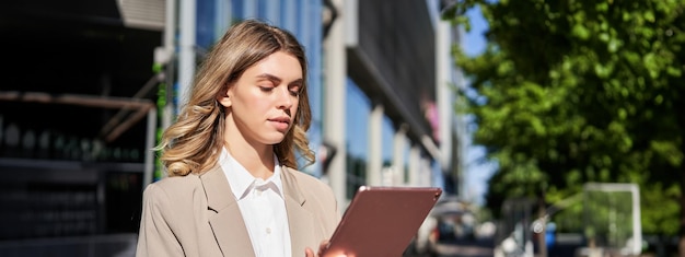 Portrait of corporate woman reads news works on her digital tablet while on her way to office stansd