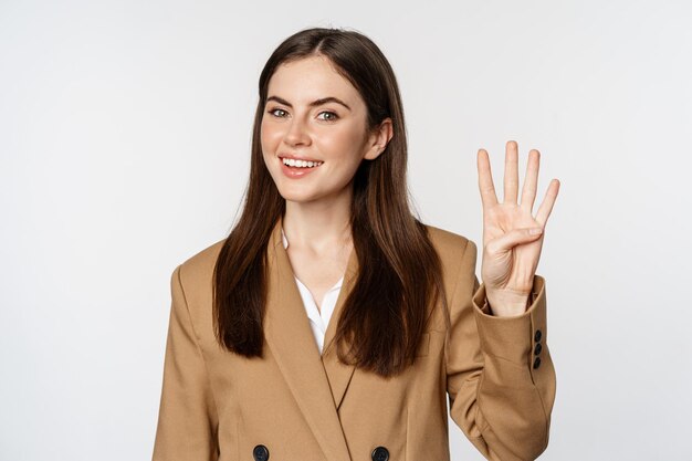 Portrait of corporate woman saleswoman showing number four fingers and smiling standing in suit over...