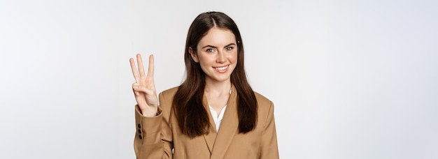 Free photo portrait of corporate woman saleswoman showing number three fingers and smiling standing in suit ove