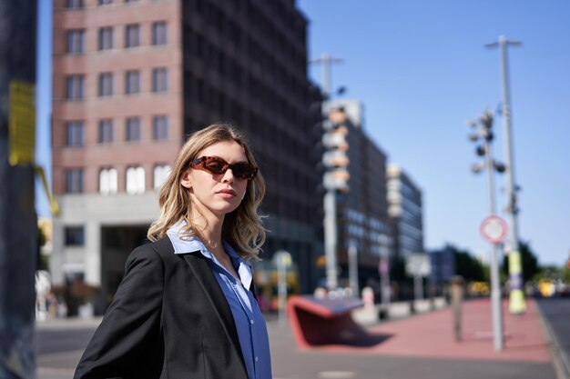 Портрет корпоративной женщины в костюме и солнцезащитных очках, стоящей на улице и выглядящей уверенно и расслабленно