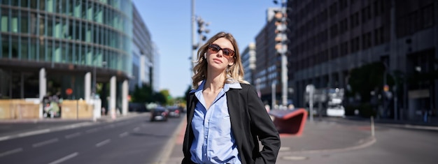 自信とリラックスした表情で通りに立つ、スーツとサングラスを着た企業女性のポートレート