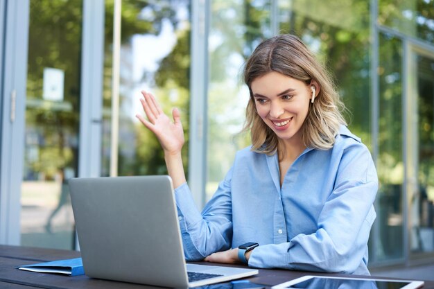 ラップトップのワイヤレスイヤホンを使ってリモートでオフィスの外で働く企業の女性のポートレート