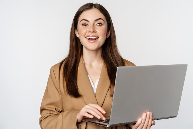 웃고 있는 자신감 넘치는 흰색 배경을 보고 있는 노트북으로 일하는 기업 여성의 초상화