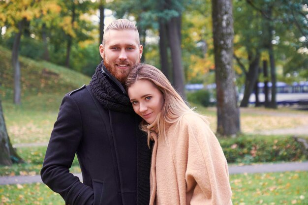 Portrait of couple on the date. Redhead bearded male hugging cute blonde female in an autumn park.