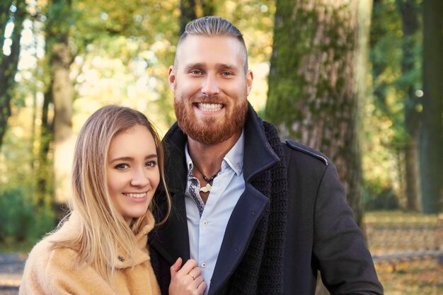 Portrait of couple on the date. Redhead bearded male hugging cute blonde female in an autumn park.