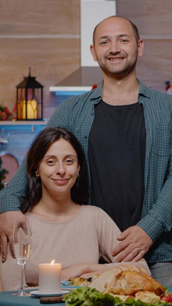 Portrait of couple at festive dinner on christmas eve. Man and woman looking at camera while enjoying holiday meal and celebration, sitting together and feeling cheerful for winter festivity