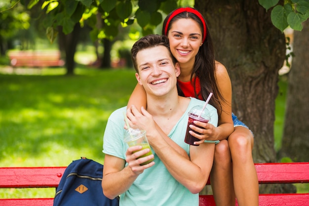 Portrait of couple sitting on bench holding smoothies in plastic cup