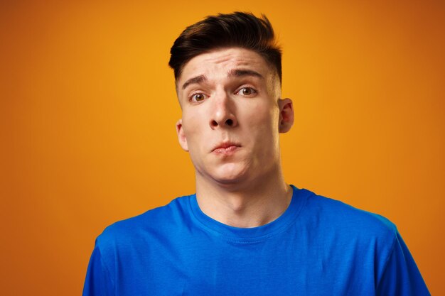 Portrait of crazy amazed young man in blue tshirt against yellow background