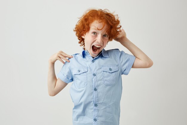 Portrait of crazy ginger kid with curly hair and freckles jumping, having fun with opened mouth and mad face expression.