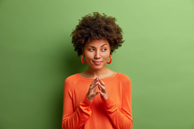 Free photo portrait of creative dark skinned young woman steepls fingers and looks mysterious aside