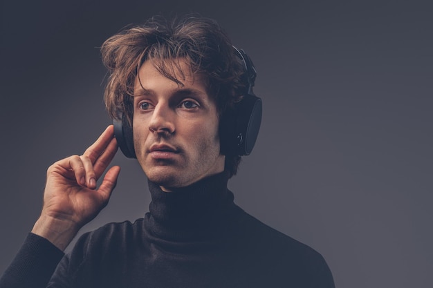Портрет творческого чувственного мужчины в черном свитере, слушающего музыку в наушниках.